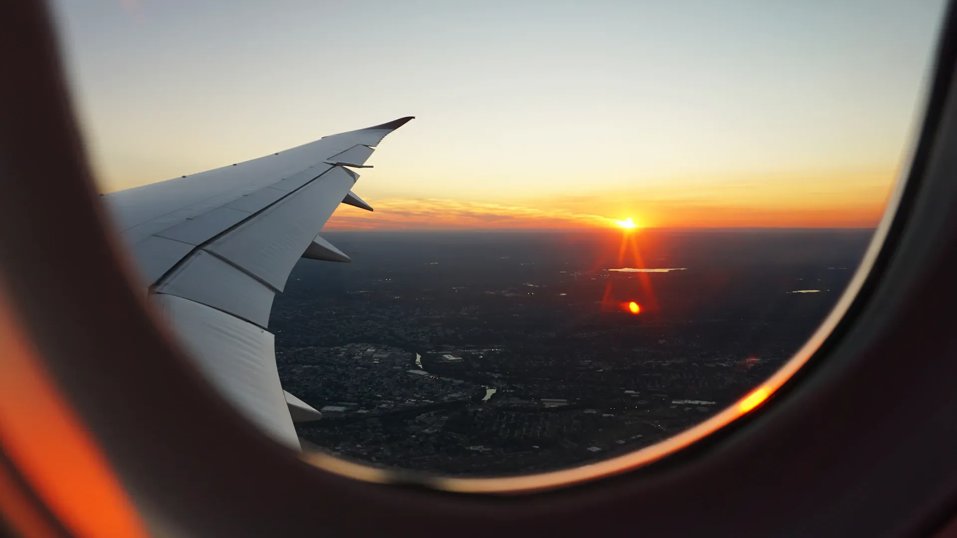 Airplane window view with dramatic clouds and golden horizon at sunset